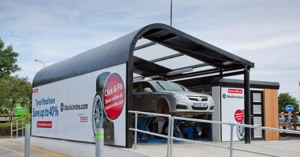 A car raised on the ramp inside a Blackcircles.com and Tesco Tyres installation bay.