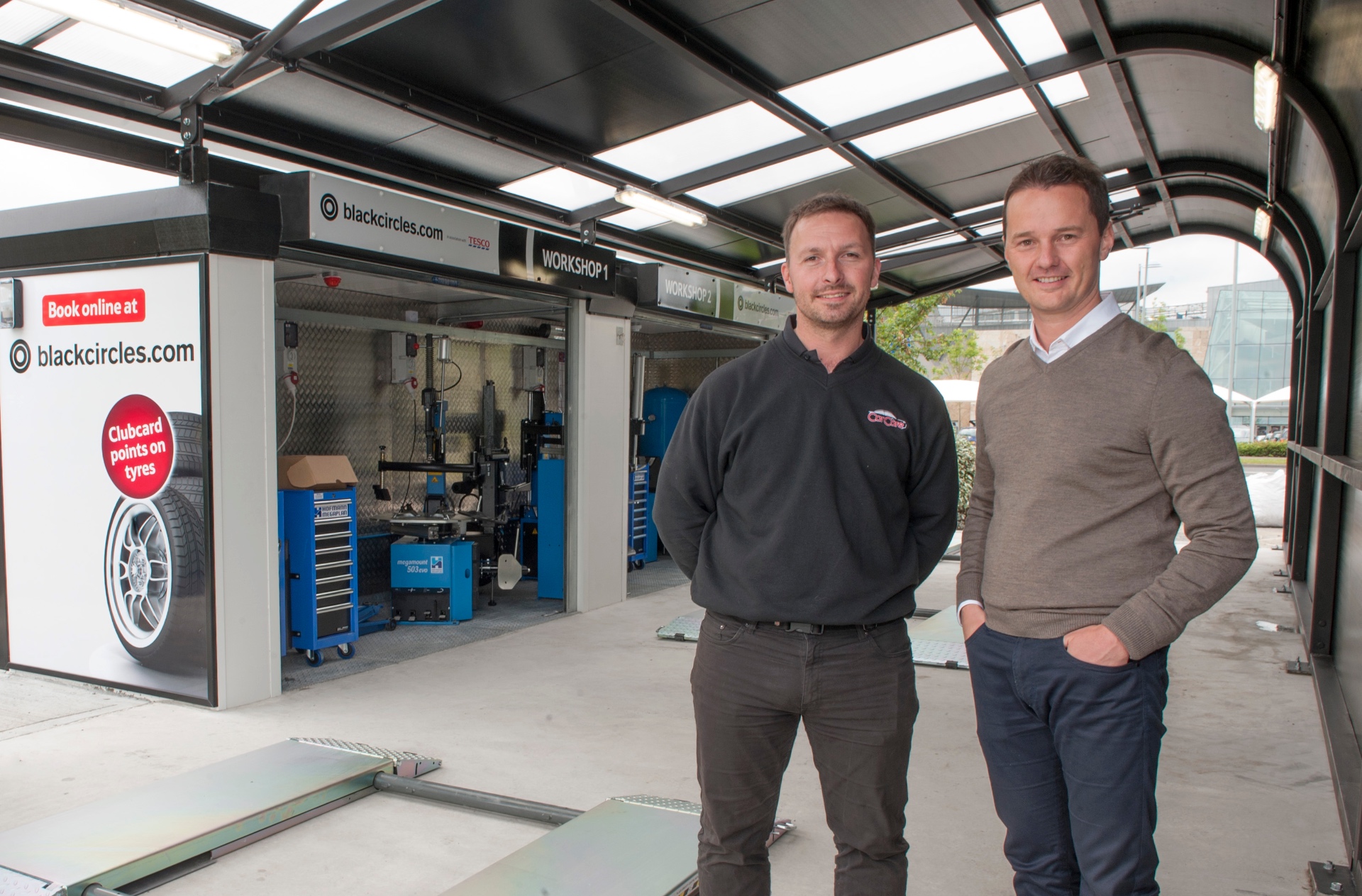 Michael Welch and a colleague standing beside a Blackcircles.com and Tesco Tyres installation bay.