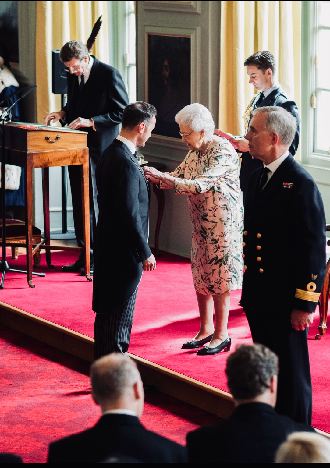 Michael Welch, in morning dress, receiving his OBE from Queen Elizabeth II at an investiture ceremony.